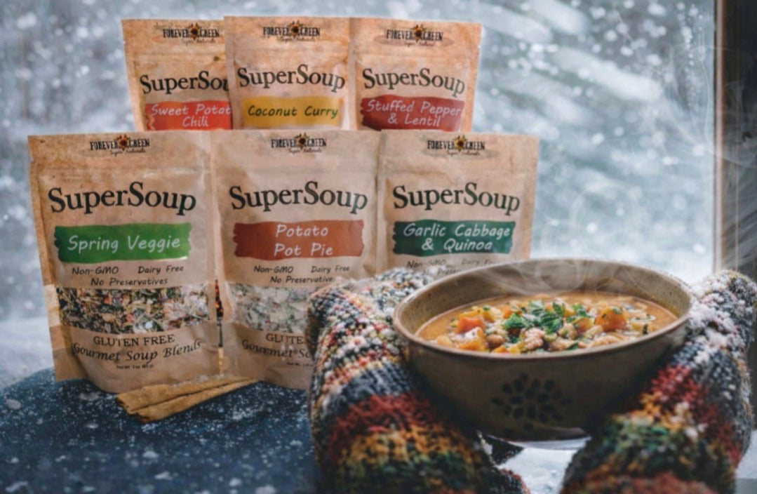 Two hands in wool mittens holding a steaming bowl of soup at a snowy window, with the SuperSoup range behind
