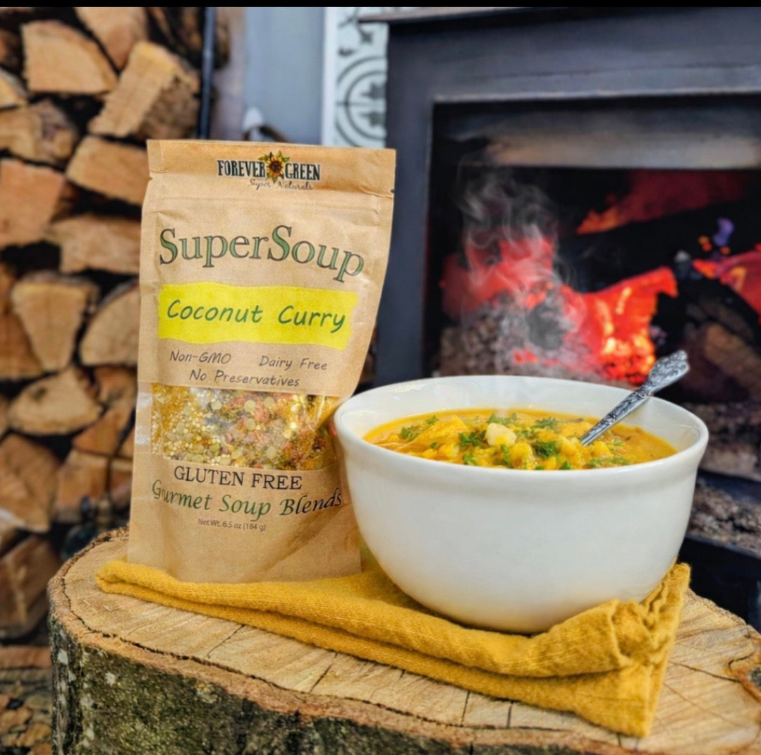 A bowl of Coconut Curry soup beside its bag, on a log slice in front of a lit fire